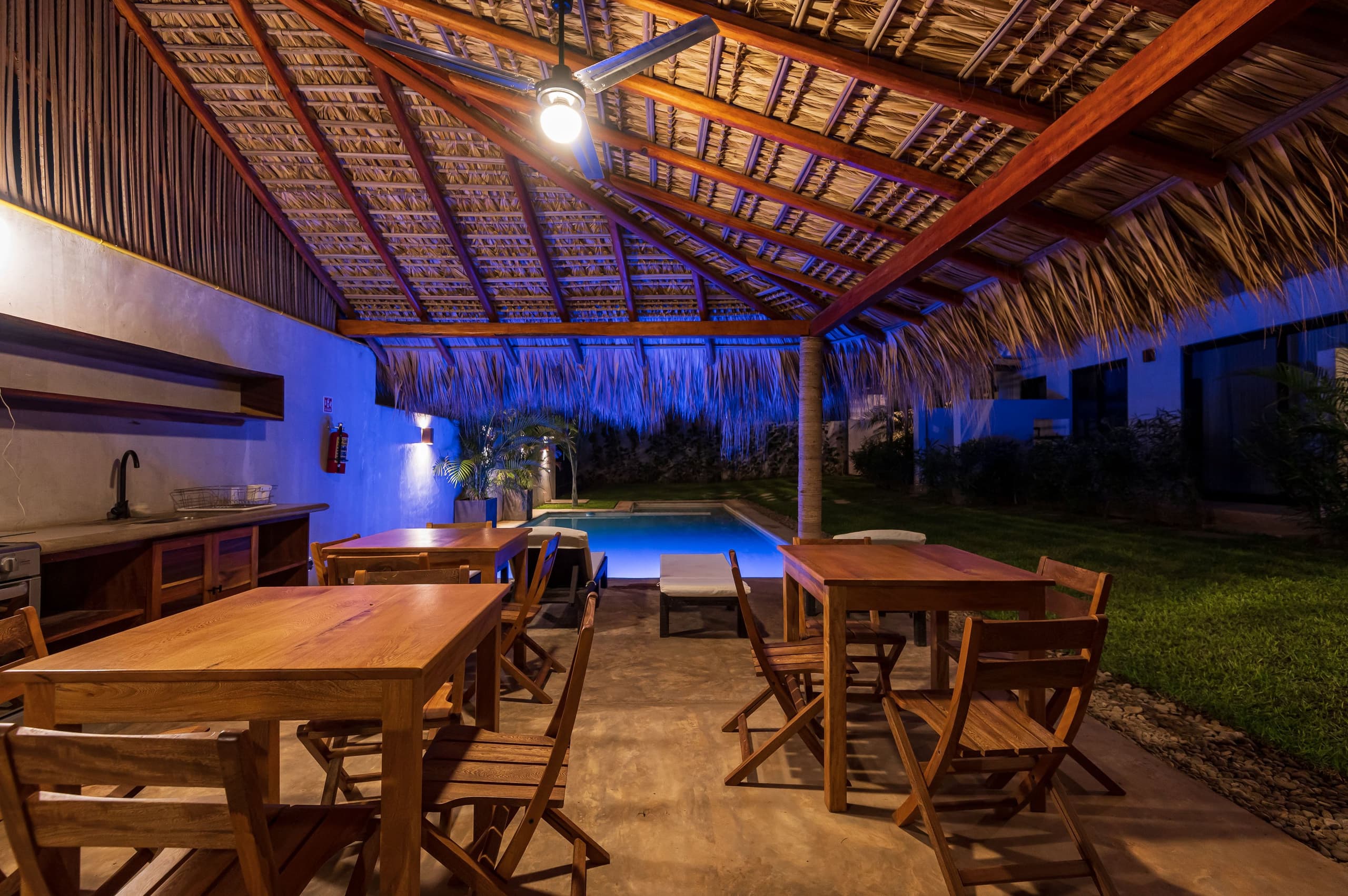 Palapa con comedor exterior iluminada de noche junto a la alberca