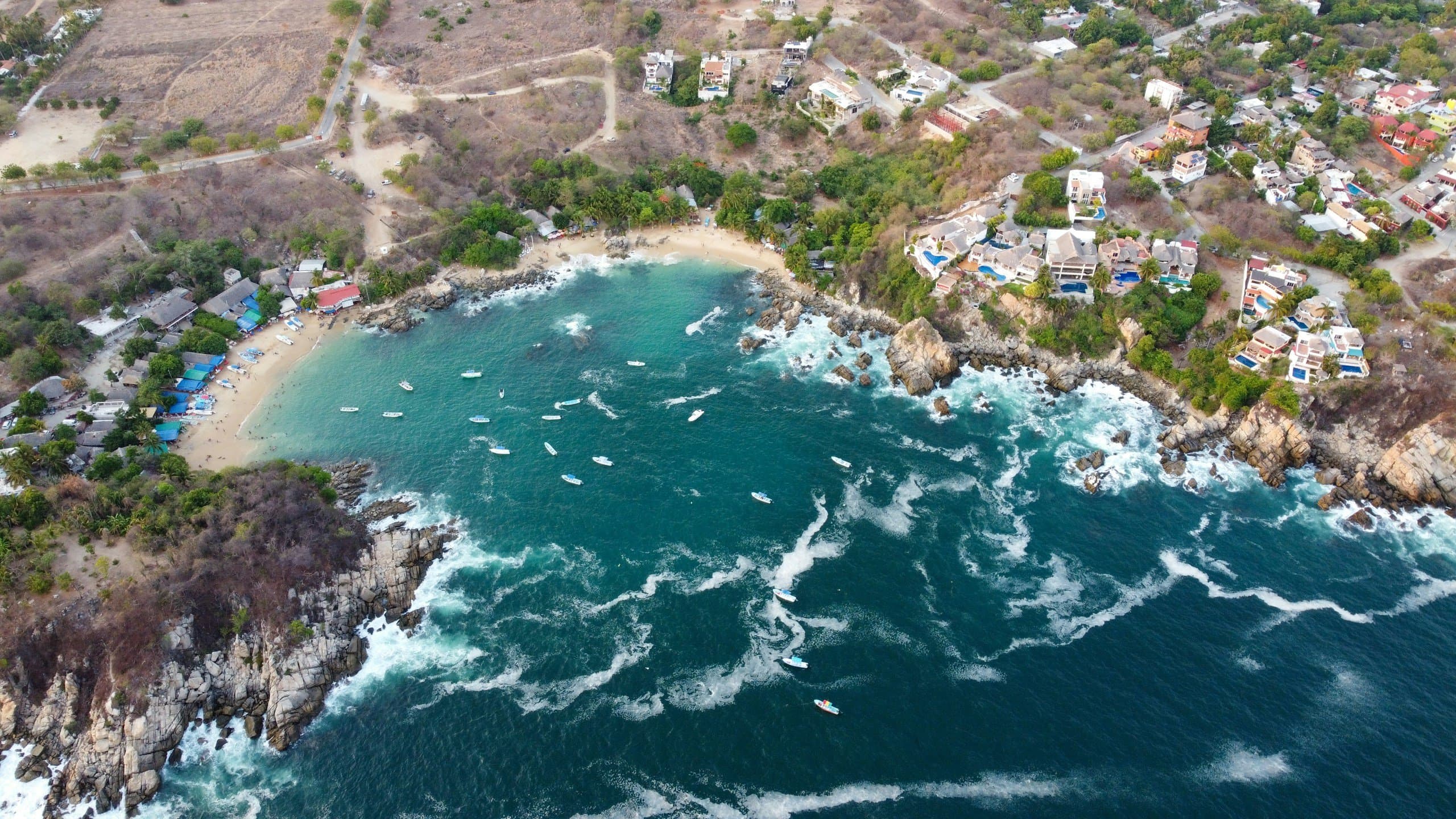 Vista aérea de una bahía de Puerto Escondido con lanchas y oleaje