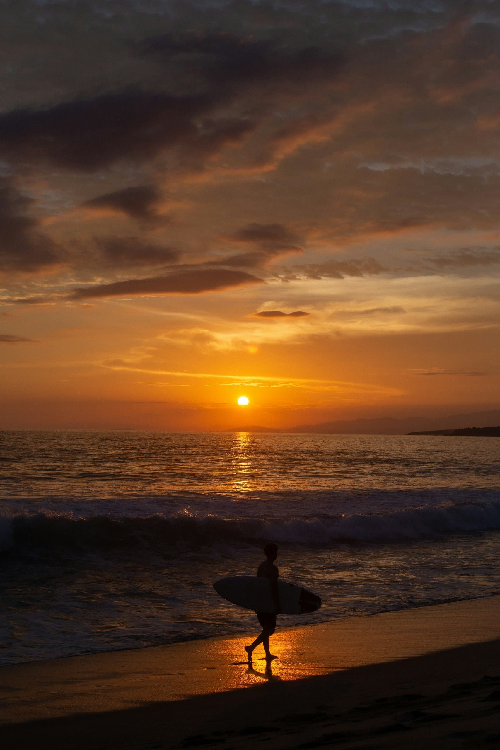 Surfista caminando por la orilla al atardecer en Puerto Escondido
